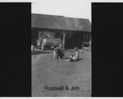 Brothers Jim and Russell Nissen with their dog sitting in a farm yard, Petaluma, California, about 1920