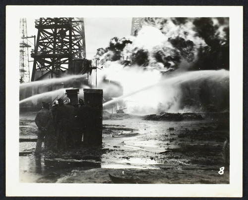 Five fire fighters controlling a hose while fighting an oil field fire (Richfield Oil Refinery explosion and fire?)