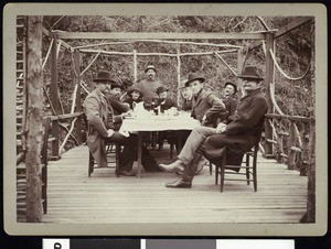A group of fishing club members, at a dinner table outside a mountain residence, ca.1910-1920