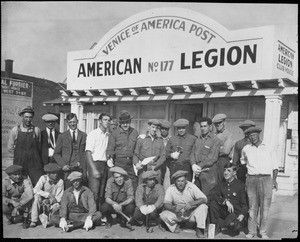 A policeman crouches with a group of 19 workers standing, crouching or sitting in front of the club house for the "American Legion, Venice of America Post, no. 177"