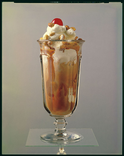 A carmel sundae top with peanuts and a cherry