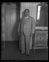 Full length portrait of General Arturo Bernal in suit, standing beside mirror and cabinet, circa 1930