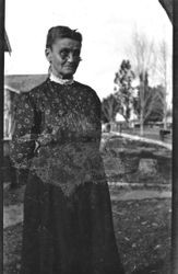 Sarah Jane White standing in what appears to be a front yard, with trees and houses in background, between 1914 and 1918