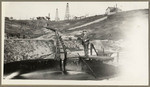 [Alfred Fuhrman standing over storage tank with pipeline in oil field area]