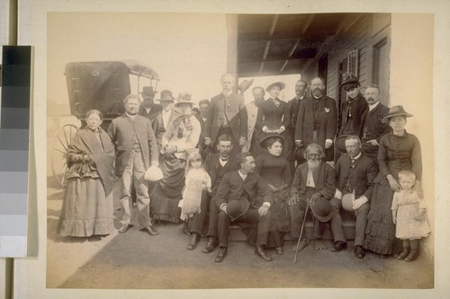 [Large group on porch of building; in group is an old Indian(?) man.]