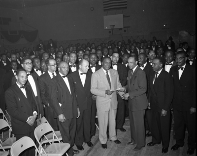 Al Fulcher (left) shaking hands with man surrounded by group of masons in basketball gym