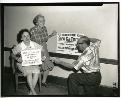 Two women and a man standing next to sign for West Oakland Oldtimers Reunion