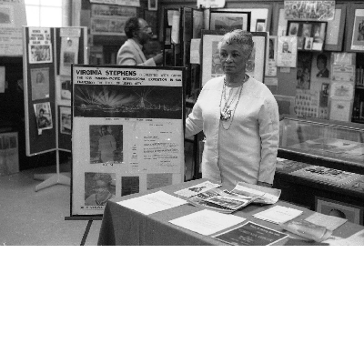 Woman standing next to Virginia Stephens exhibit poster at the East Bay Negro Historical Society