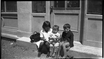 Three children sitting in doorway of building