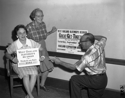 Two women and a man standing next to sign for West Oakland Oldtimers Reunion