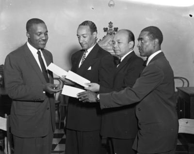 Three men handing unidentified man checks