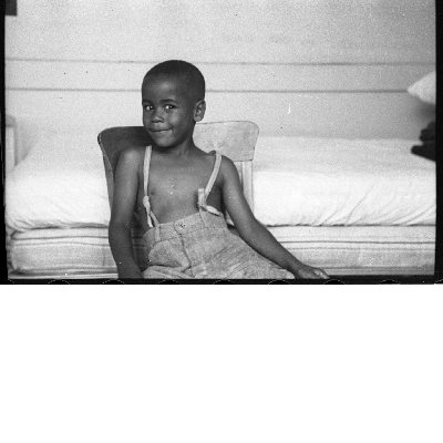 Boy in overalls sitting in chair smiling