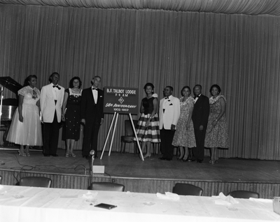 Men and women standing on stage next to B.F. Talbot Lodge F. & A.M. 50th anniversary 1902-1957 sign
