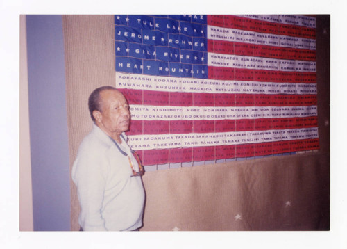 Man standing next to memorial on American flag dedicated to incarceration of Japanese Americans during World War II
