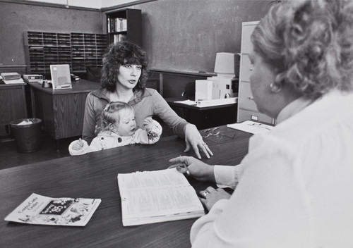 Photograph of woman with baby speaking with administrative official