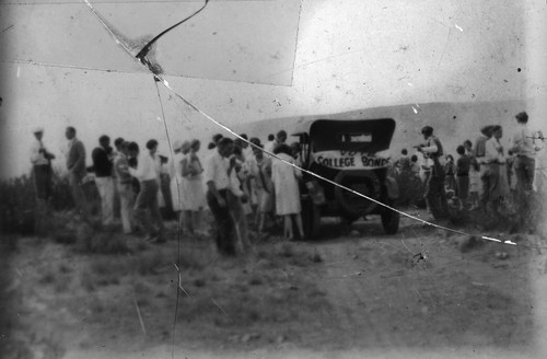 [A crowd standing outdoors next to a car]