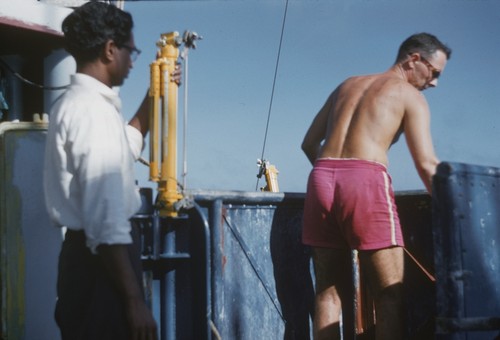 C. Balarama Murty (left) ready with another Nansen bottle and Jan B. Lawson (right) of the Scripps Institution of Oceanography's Swan Song Expedition (1961), inspecting the line with the Nansen bottles aboard the R/V Argo. This expedition explored the North Pacific at the equator and Eastern Tropical Pacific on the research ship Argo. The expedition collected large water samples for analysis, studied the Cromwell Current (Pacific Equatorial Undercurrent), and undertook a limited biological program for the Inter-American Tropical Tuna Commission.1961
