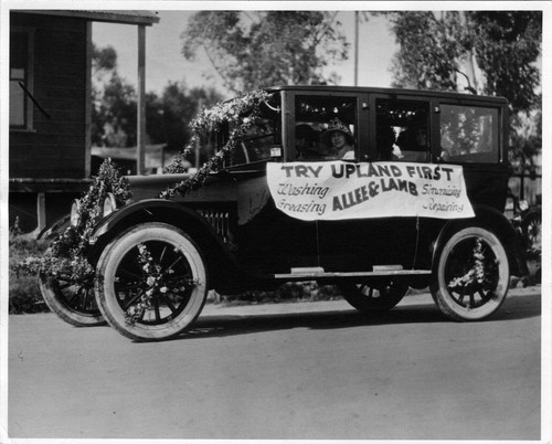 Upland Photograph Events; Parade: woman seated in driver's seat of automobile advertising Try Upland First Allee & Lamb washing greasing simonizing repairing