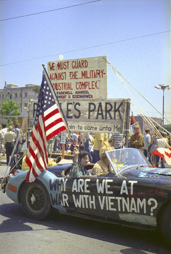 Car and flag in front of People's park says "Why are we at war with Vietnam?"