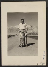 Manzanar, Calif.--Grandfather of Japanese ancestry teaching his little grandson to walk at this War Relocation Authority center for evacuees. Photographer: Lange, Dorothea Manzanar, California