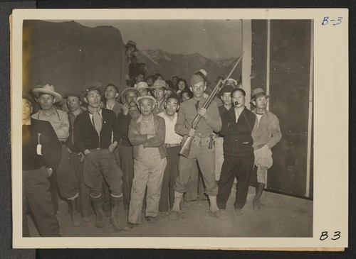 Manzanar, Calif.--While military policeman stands guard, this detachment watches arrival of evacuees of Japanese ancestry at this War Relocation Authority center. Photographer: Albers, Clem Manzanar, California