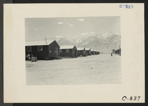 Manzanar, Calif.--Far end of barrack row looking west to the desert beyond with the mountains in the background. Evacuees at this War Relocation Authority center are encountering the terrific desert heat. Photographer: Lange, Dorothea Manzanar, California