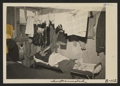 An evacuee resting on his cot after moving his belongings into this bare barracks room. Army cot and mattress are the only things furnished by the government. All personal belongings were brought by the evacuees. Photographer: Albers, Clem Manzanar, California