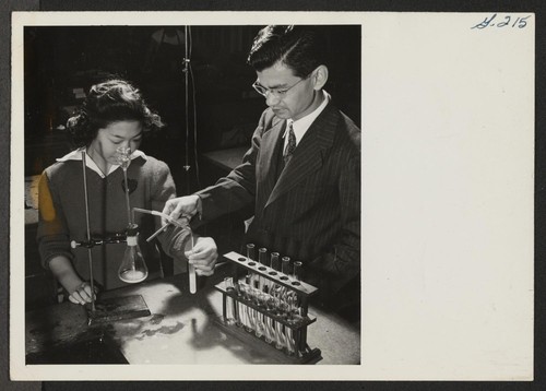 Scene in the Chemistry class at the Heart Mountain High School, as Kaoru Inouye, instructor, is showing student Sumi Tam[...] a step in one of the Chemistry experiments. Photographer: Iwasaki, Hikaru Heart Mountain, Wyoming