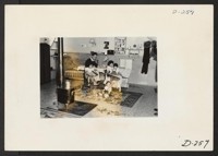 An evacuee family spends a quiet evening in their barracks. The decoration of this apartment is quite typical and shows the home made furniture, shelves, bookcases and other furniture. Photographer: Stewart, Francis Newell, California