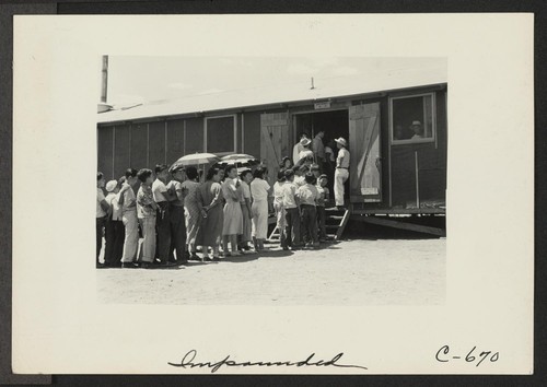 Part of a line waiting for lunch outside the mess hall at noon. Photographer: Lange, Dorothea Manzanar, California