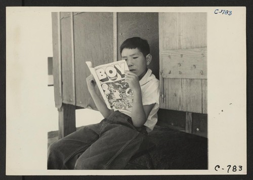 Manzanar, Calif.--Evacuee boy at this War Relocation Authority center reading the Funnies. Photographer: Lange, Dorothea Manzanar, California