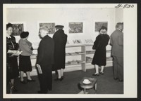 Spectators are viewing paintings and drawings of relocation center life by Miss Mine Okubo, Nisei, who resettled to new York