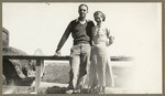 [Young man and woman posing near fence]