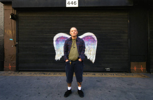 Unidentified man in a plaid shirt posing in front of a mural depicting angel wings