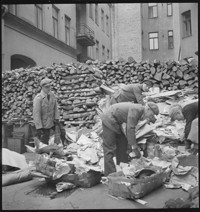 Cleaning attics [Men and boys going through piles of household things in the street]