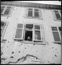[Micellaneous Village: possibly Ammerschwihr. Old woman at window of bullet-riddled building]