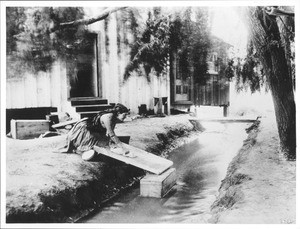 Woman washing clothes on board at a stream on Camulos Ranch illustrating wash day for the book, Ramona, ca.1885