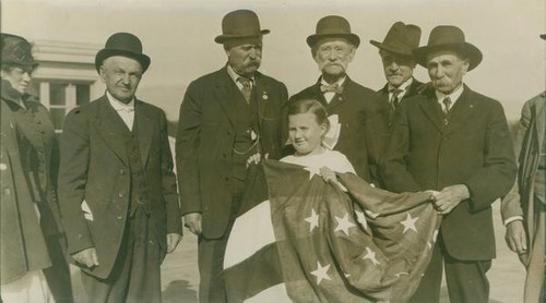 Group of adults standing behind a young girl holding an American flag