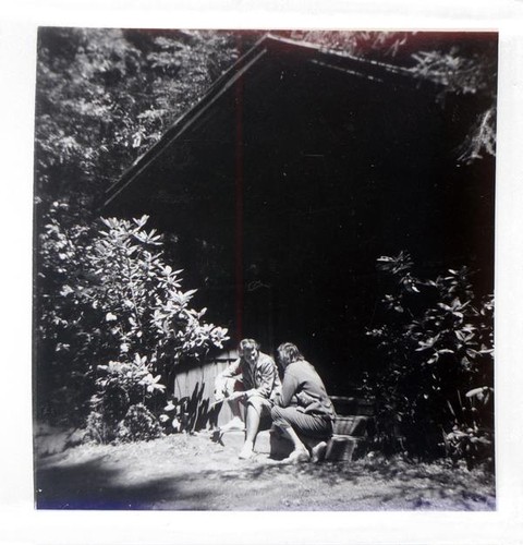 Two women sitting and talking on the steps of a building in the forest