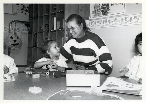 Woman sits with a girl playing with legos