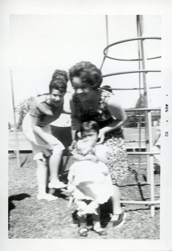 Little girl with a doll and teenage girls standing by a jungle gym