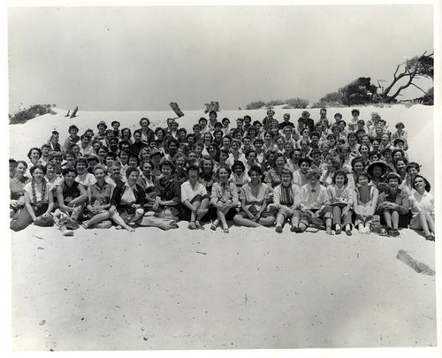 Large group portrait of women sitting in the sand probably at Asilomar