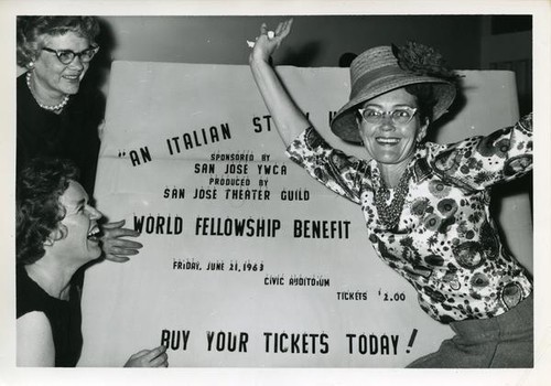 Three women pose with a large poster