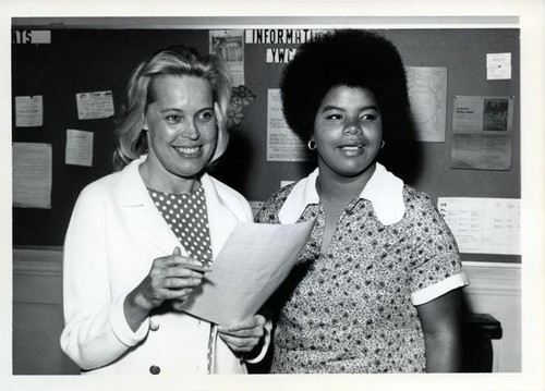 Elaine Mitchell and another woman in front of the YWCA's bulletin board