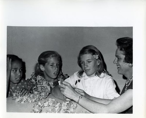 Mrs. Mary Mahle helps three girls make leis