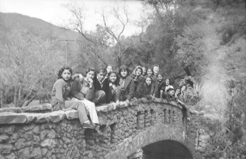 Teenage girls posing along the wall of a stone bridge