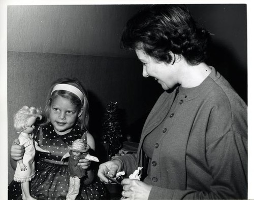 Woman looking at a little girl with two dolls