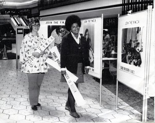 Elaine Mitchell and another woman walking past YWCA posters