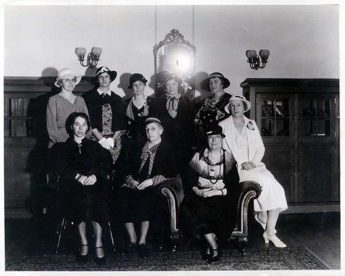 Group portrait of women posing indoors wearing dresses and hats