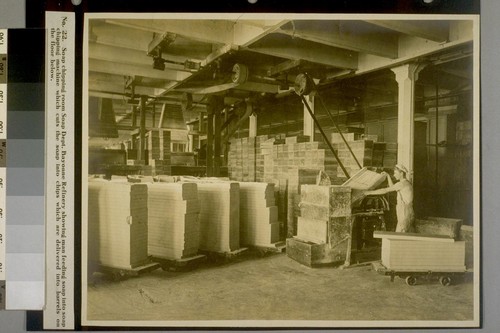 Soap chipping room Soap Dept. Bayonne Refinery showing man feeding soap into soap chipping machine which cuts the soap into chips which are delivered into barrels on the floor below